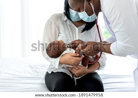 African doctor wearing surgical mans and using a stethoscope, checking the respiratory system and heartbeat Of a 12-day-old baby newborn, who is half African half Thai, to Infant health care concept.