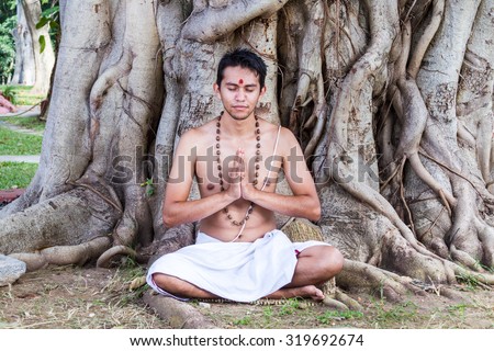 A young brahmin sits in meditation under a banyan tree in India