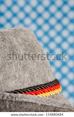 oktoberfest german hunting hat with three ropes colored in the national colors of Germany - isolated on typical bavarian colored background