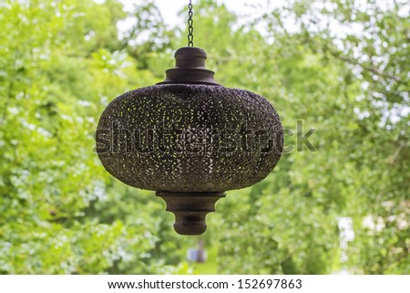 A vintage porch light hanging with a view of trees in the background.