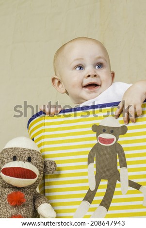 An infant boy sitting in a sock monkey box smiling.