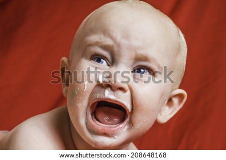 An infant boy crying with birthday cake on his face.