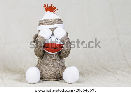 A close shot of a sock monkey playing peek-a-boo with their hand covering its eyes.