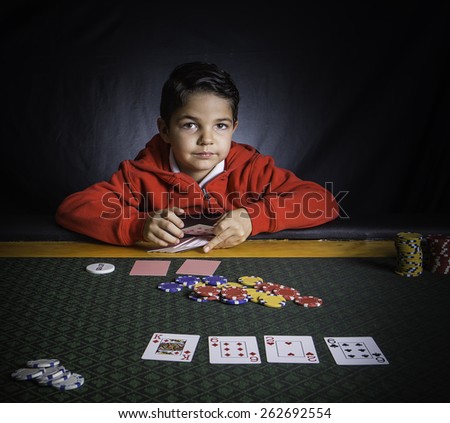 A young boy sitting at a poker table gambling playing cards with a black background