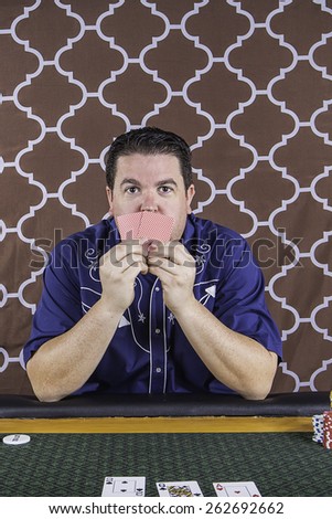 A man sitting at a poker table gambling playing cards against a brown background