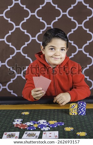A young boy sitting at a poker table gambling playing cards with a brown background