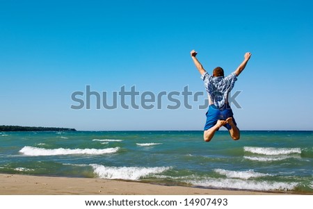 Happy man jumping over sea. Sand beach and blue water. Summer, vacation.