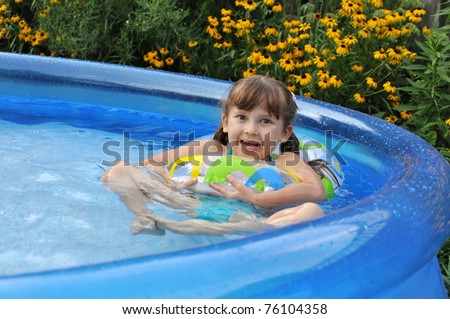 Happy girl in a swimming pool on backyard. Summer time, hot day.