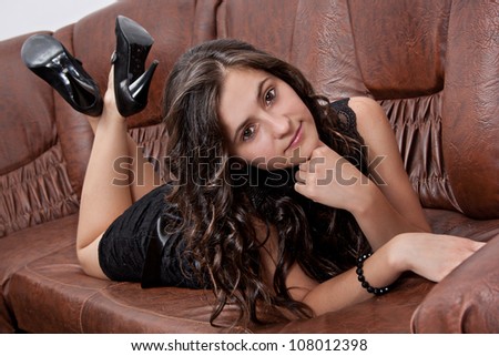 Pretty brunette in black dress laying on leather sofa