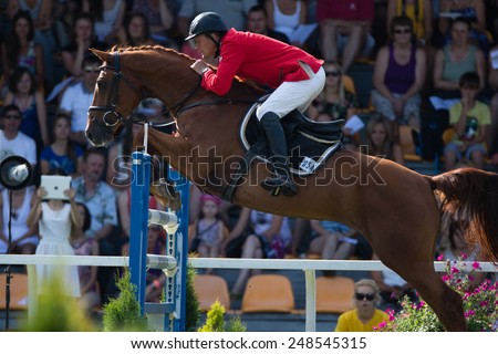 RIGA, LATVIA - JULY 27: Rider Vasil Ivanou with horse Chiort Poberi jumps over obstacle with spectators at background at CSI2*-W/ CSIYH1* - RIGA-2014 on JULY 27, 2014 in RIGA