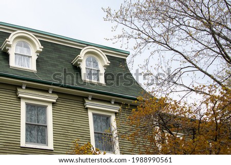 A vintage green wooden building with cream color trim, double hung windows, dormers, a green shingled roof. It's an old wooden home with multiple stories and a leafless tree and blue skies.  Stock foto © 