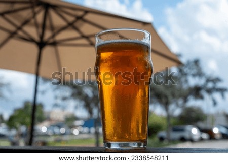 A clear pint drinking glass filled with cold froth from a lager ale. The Irish red ale pint sits on the edge of a metal patio table at a microbrewery. There's a patio umbrella in the background. Stok fotoğraf © 
