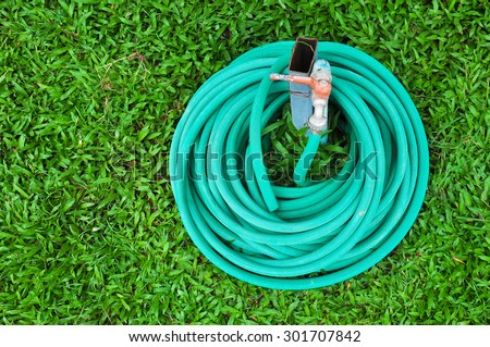 green garden hosepipe, green plastic sprayer hose for irrigation laying in garden on green grass, Garden hose coiled on green grass