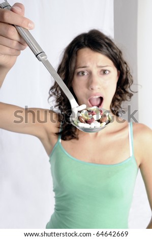 Pretty young woman holding spoon with pile of pills looking skeptical. Concept shot for drug abuse or pharmaceutical industries.