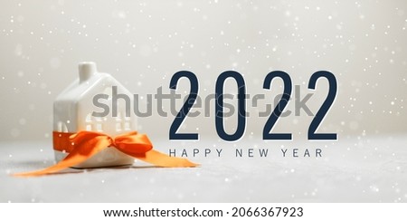 Merry christmas and 2022 happy new year horizontal banner with small toy model house wrapped in red satin ribbon on a white background