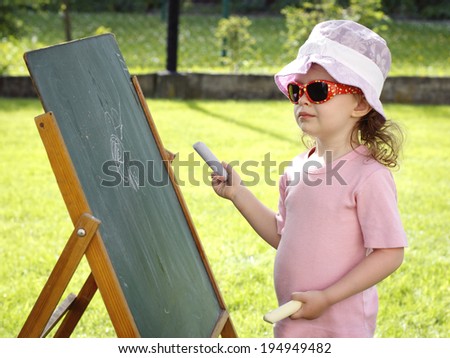 Little girl drawing on the board in the garden