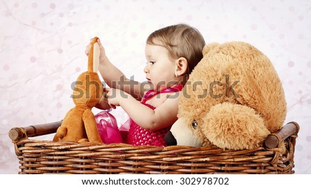 Little baby girl playing with plush toys in wicker basket