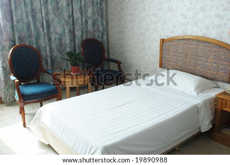 The bed and armchairs of a hotel double room.