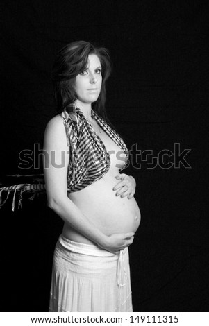 Pregnant woman side-on with checked scarf and white skirt holding tummy in black and white