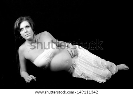 Pregnant woman lying on her side looking pensive wearing white skirt with black background in black and white