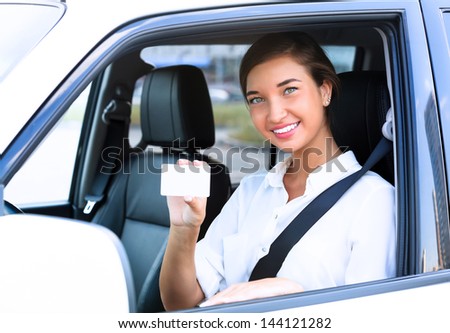Happy girl in a car showing an empty white card for your message