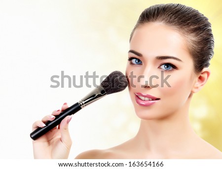 Pretty woman with cosmetic brushes against an abstract blurred background