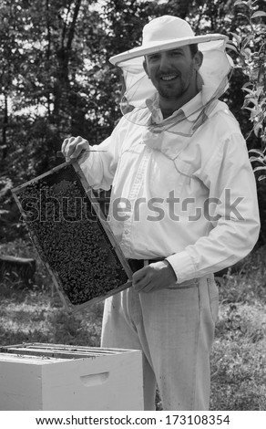 Young beekeeper smiling and showing his bee colony
