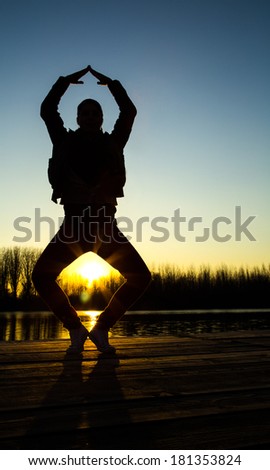 Silhouette of young woman at sunset on lake doing yoga.