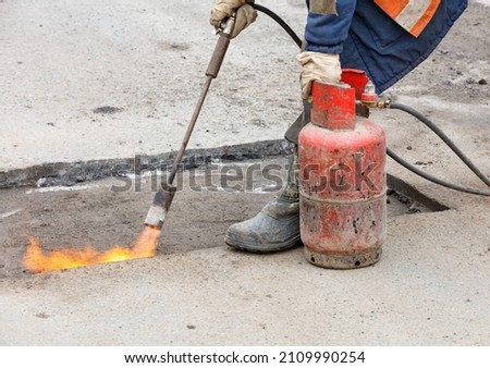 Pothole repair of the road. The worker, using a gas burner and a propane tank, heats up the asphalt surface for better bitumen adhesion. 商業照片 © 
