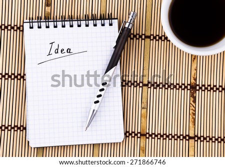 Idea written in notepad, Pen and Coffee Cup on Bamboo Background.