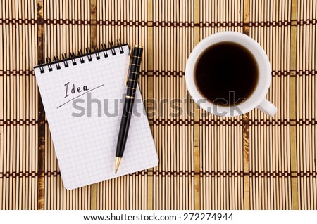 Idea written in notepad, Pen and Coffee Cup on Bamboo Background.