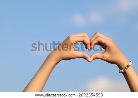 A woman raises her hand above her head to make a heart symbol on the background of the bright morning sky because the heart symbol signifies love, friendship and kindness to one another. Stock foto © 