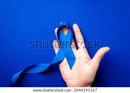 Blue ribbon. Awareness prostate cancer of men health in November. Blue ribbon in hands isolated on deep blue background. Symbol of oncology affected man. Copy space