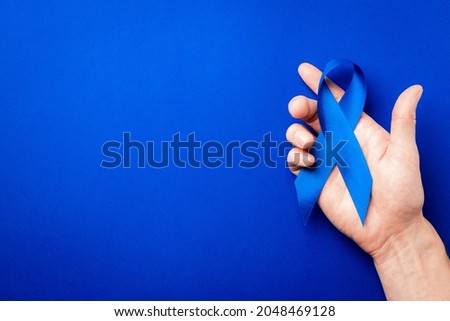 November. Blue ribbon in hands isolated on deep blue background. Awareness prostate cancer of men health in November. Supporting people living and illness.
