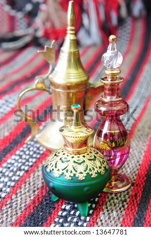 Egyptian perfume bottles arranged on a hand-woven Omani rug. A copper replica of an old coffee pot is faded in the background.