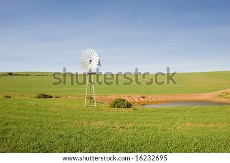A traditional windmill turning in the wind and pumping water out of the ground into a catchment dam to the right.