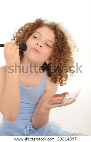 A gorgeous little girl with curly hair in the studio, wearing a ballet outfit and playing with make up, white background.