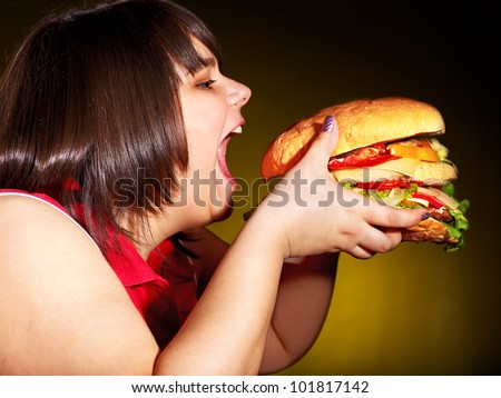 Overweight hungry woman eating hamburger.