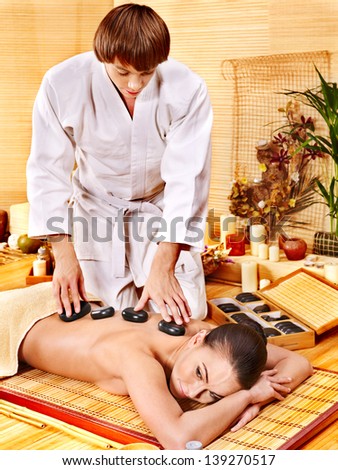 Woman getting stone therapy in bamboo spa. Male massage therapist.