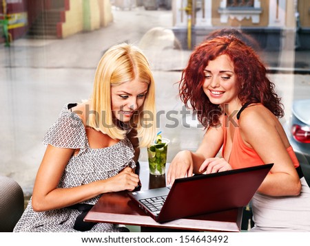Two women at laptop drinking cocktail in a cafe.