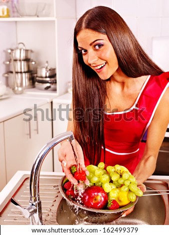 Happy woman washing fruit at kitchen.