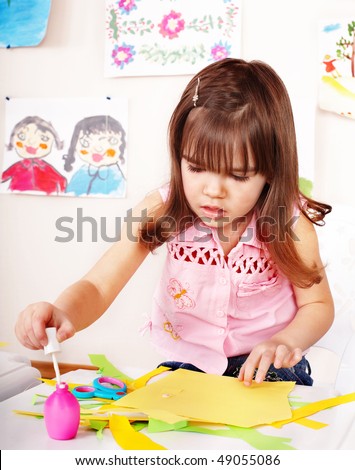 Child with scissors cut paper in play room. Preschool.