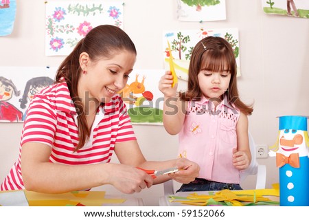 Child with scissors cut paper in play room. Preschool.