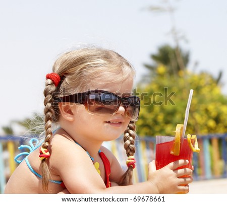 Little girl in glasses and red bikini on playground drink  juice.
