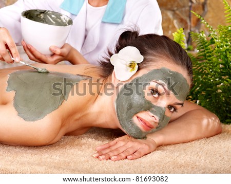 Beautiful girl having clay body mask apply by beautician.