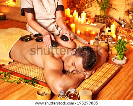 Man getting stone therapy massage in bamboo spa.