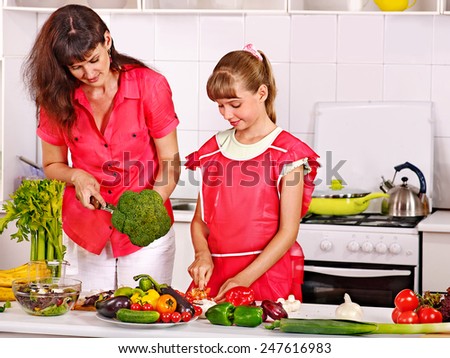 Mother and daughter cooking food at kitchen.A lot of vegetables and herbs on table