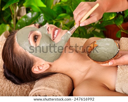 Woman with clay facial mask in beauty spa.Towel under the neck