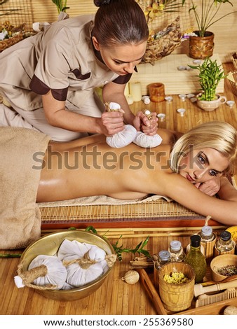 Blond woman getting herbal ball massage in spa. Masseuse standing on tracks