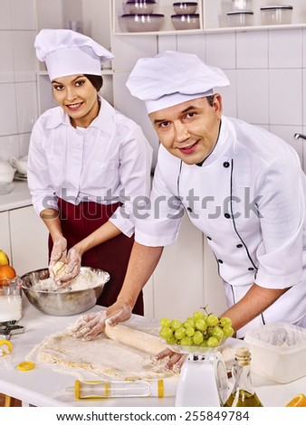 Happy woman and man in uniform cooking dough .